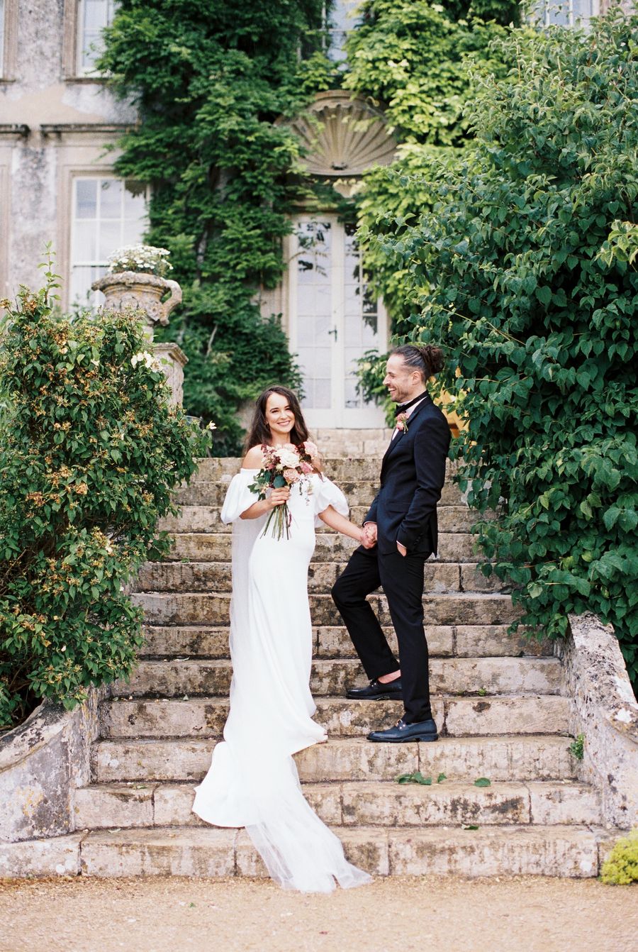 Bride and groom holding hands on stone steps, Cotswolds wedding venue